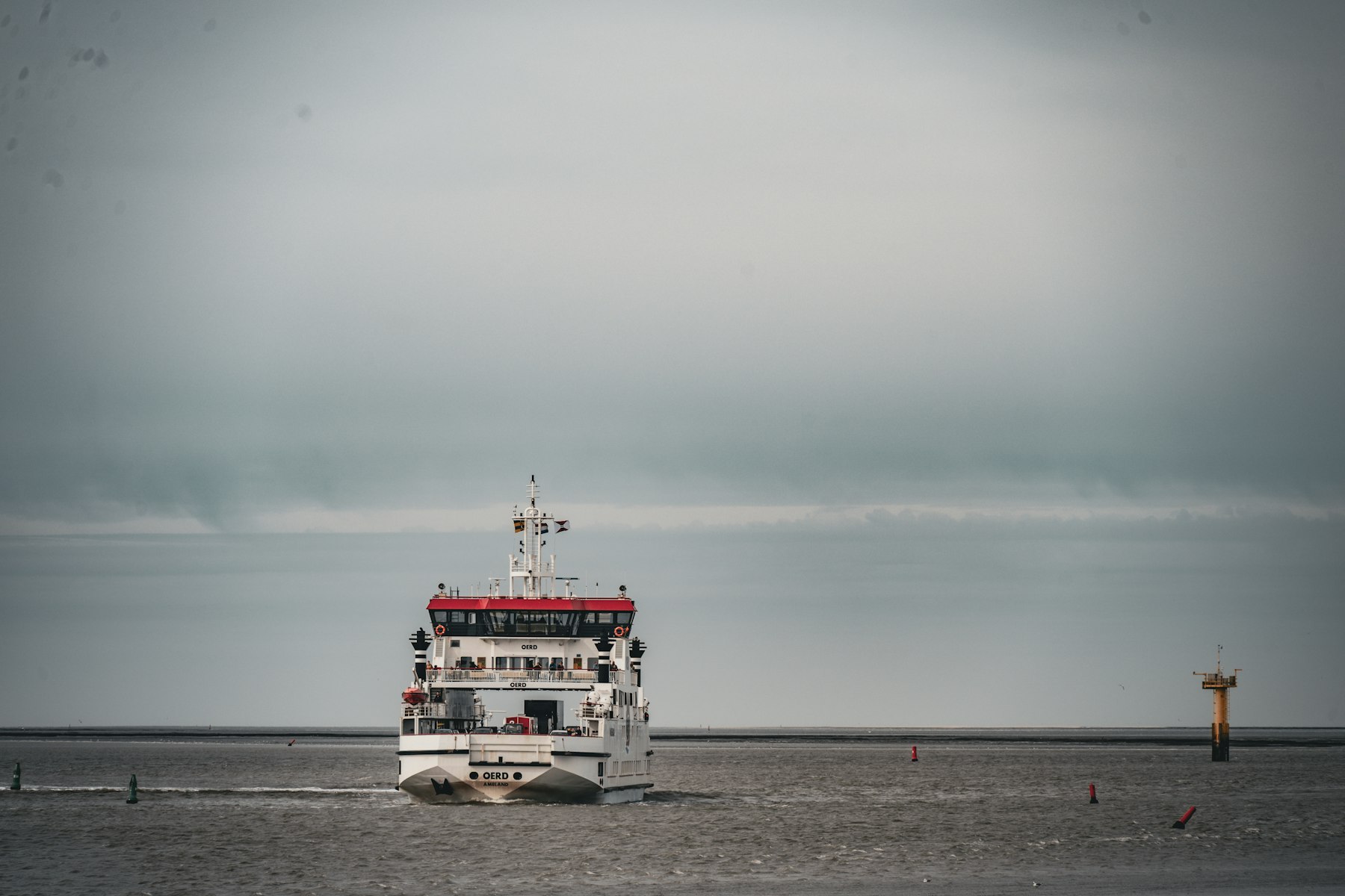 A white and red ferry on calm water under a grey sky